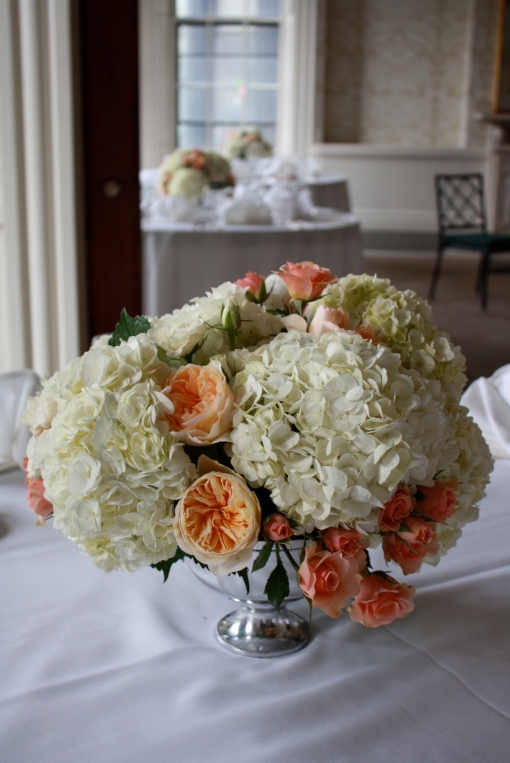 Peach and ivory flowers complement the silver of the table and container 